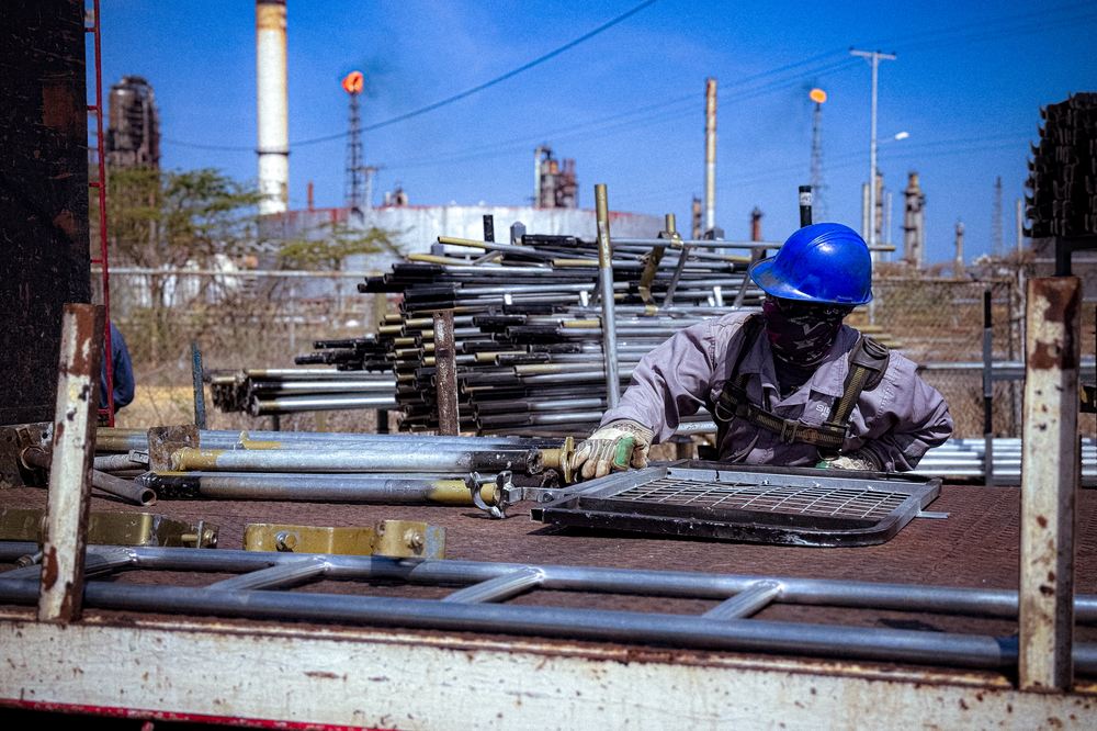 Andamiero preparando material de andamiaje con la refinería al fondo